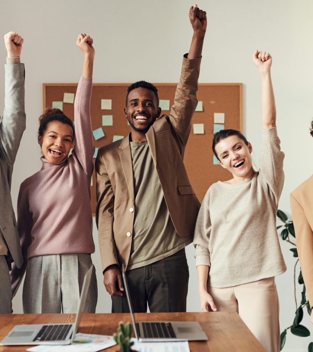 A diverse team celebrating success with raised hands in a modern office setting.