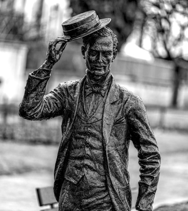 Elegant bronze statue of a man in a suit tipping his hat, captured in black and white.